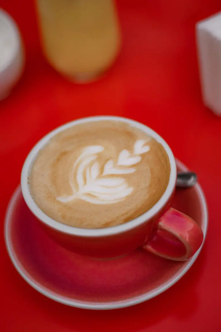 A beautifully crafted cappuccino with intricate latte art served on a vibrant red table.