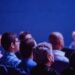 An attentive group of adults seated at an indoor conference, focusing on a presentation.