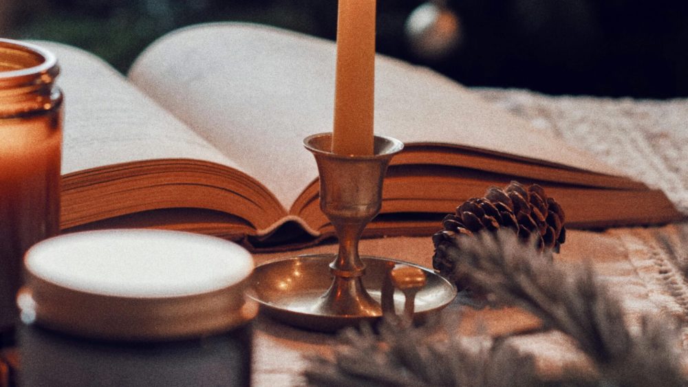 Warm scene with open book, lit candle, and festive decor, perfect for holiday season ambiance.